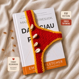 May include: A handmade crochet bookmark featuring a red fabric body with a yellow border, adorned with four small white cowrie shells along the side. The bookmark is placed on a book with text that reads PDF PATTERN, VIDEO TUTORIAL, and FUNNY BOOKMARK.
