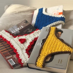 Può includere: Accessori per libri all'uncinetto in bianco, rosso, blu e giallo. L'immagine mostra tre segnalibri a perizoma e un segnalibro blu. I segnalibri sono posizionati sopra i libri. I segnalibri sono fatti a mano e hanno un design unico.