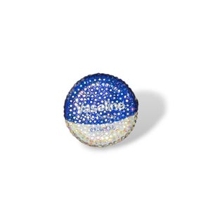 May include: A bedazzled, round container of Vaseline Original. The top half is dark blue with white dots, the bottom half is white. The text "Vaseline Original" is visible. The container is covered in small, sparkling rhinestones.