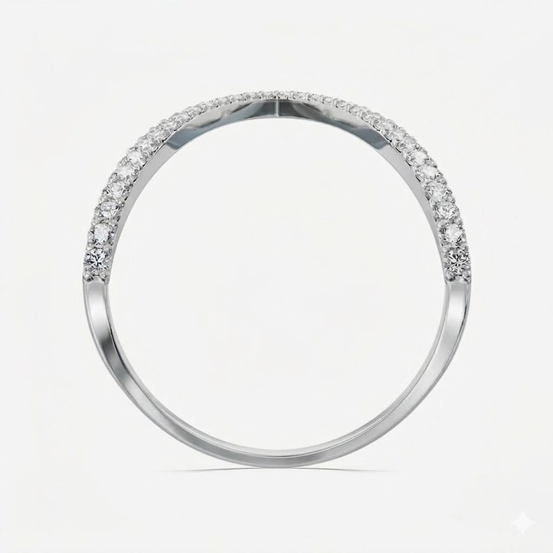 May include: A silver ring with a curved design, set with small, sparkling gemstones along the top half of the band. The ring is displayed against a plain white background, highlighting its elegant simplicity.