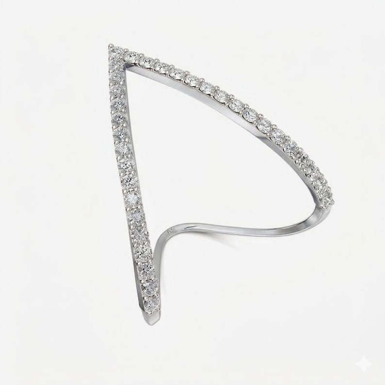 May include: A silver-toned ring with a unique, open design. The ring features a V-shape and a curved band, both encrusted with small, sparkling clear stones. The stones are evenly spaced, creating a continuous line of brilliance.