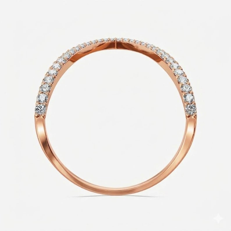 May include: Rose gold ring with a curved design, set with a row of small, sparkling white gemstones. The ring has a smooth, polished finish and a delicate, elegant appearance. The gemstones are evenly spaced along the top curve of the ring.