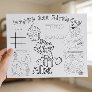 May include: A white activity sheet with the text "Happy 1st Birthday" and the name "Alba". The sheet features a tic-tac-toe grid, a cupcake, and cartoon characters. It includes connect-the-dots and maze activities.