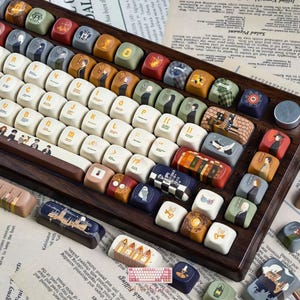May include: A mechanical keyboard with a dark wood frame and custom keycaps featuring various illustrations, including characters, magical objects, and symbols. The keys are a mix of cream, brown, green, blue, and red, with some displaying letters.
