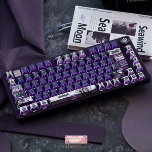 May include: A mechanical keyboard with a dark purple frame and backlit keys. The keycaps feature a mix of solid purple and custom graphic designs, including Japanese text and anime-style illustrations. A circular knob is located on the top right corner.