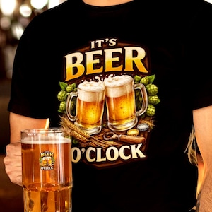 Peut inclure: T-shirt noir avec l'inscription "IT'S BEER O'CLOCK" et un graphisme de deux chopes de bière. La photo montre une personne tenant un verre de bière. L'arrière-plan est un bar avec un éclairage chaleureux.