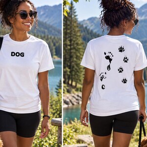 Może przedstawiać: Biały t-shirt z krótkim rękawem z napisem DOG wydrukowanym na czarno na klatce piersiowej. Tył koszulki przedstawia graficzny wzór czarnych odcisków łap oraz jeden odcisk ludzkiej stopy, tworząc kontrast z białym materiałem.
