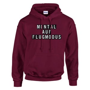 Op de afbeelding: Een bordeauxrode hoodie met de tekst "MENTAL AUF FLUGMODUS" in witte blokletters. De hoodie heeft een capuchon met trekkoord en een voorzak. De merknaam "Gildan" is zichtbaar.
