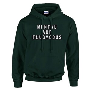 Op de afbeelding: Donkergroene hoodie met de tekst "MENTAL AUF FLUGMODUS" in witte blokletters. De hoodie heeft een voorzak en een capuchon met trekkoord. Het Gildan-logo is zichtbaar op de capuchon.
