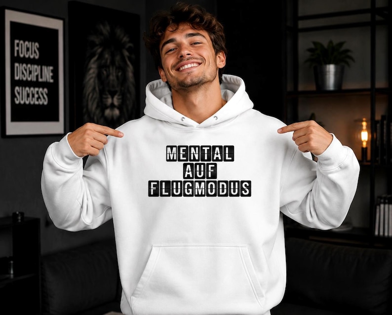 Op de afbeelding: Witte hoodie met een voorzak en een trekkoord. De tekst "MENTAL AUF FLUGMODUS" staat in zwarte blokletters op de borst. De persoon op de foto wijst naar de tekst.