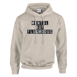 Op de afbeelding: Een lichtbeige hoodie met een capuchon met trekkoord en een kangoeroezak. De voorkant van de hoodie heeft de tekst "MENTAL AUF FLUGMODUS" in zwarte blokletters. De hoodie is gemaakt van een zacht, comfortabel materiaal.