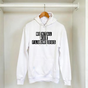 Op de afbeelding: Witte hoodie met een voorzak en een capuchon met trekkoord. De hoodie toont de tekst "MENTAL AUF FLUGMODUS" in zwarte blokletters. De hoodie hangt aan een houten hanger.