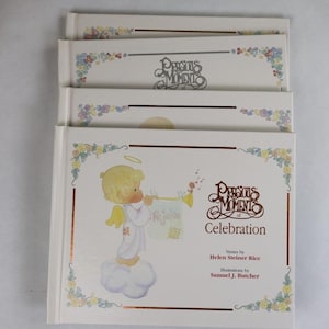 Peut inclure: Pile de trois livres "Precious Moments of Celebration". Les couvertures blanches sont bordées d'or et ornées de motifs floraux. La couverture présente un ange jouant de la trompette et le titre.