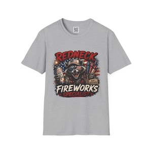 May include: A gray t-shirt featuring a raccoon wearing an American flag bandana and a hat. The raccoon is holding a can and fireworks, with the words "Redneck Fireworks Specialist" in a patriotic design.