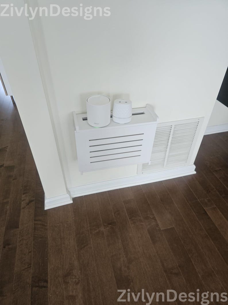 Puede incluir: Una cubierta blanca para ventilaci&oacute;n con un estante que sostiene dos dispositivos electr&oacute;nicos blancos. El estante tiene listones horizontales. La pared es blanca y el suelo es de madera marr&oacute;n oscuro. El texto "ZivlynDesigns" est&aacute; en las esquinas superior izquierda e inferior derecha.