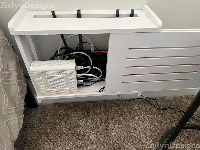 Puede incluir: Consola de medios de madera blanca con un compartimento incorporado para electr&oacute;nica. La consola cuenta con una balda superior, una puerta de lamas y un compartimento que alberga un m&oacute;dem, un router y varios cables. El dise&ntilde;o incluye el texto "ZivlynDesigns".