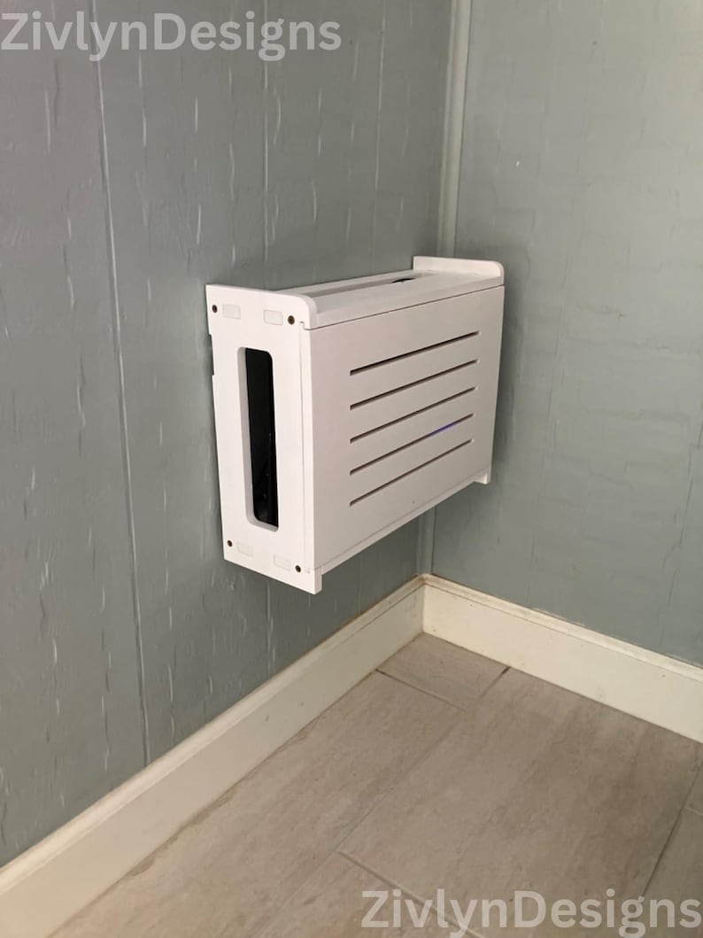 Puede incluir: Una caja blanca rectangular montada en la pared con una parte frontal ranurada y una gran abertura lateral. La caja est&aacute; montada en una pared gris en una esquina. El texto "ZivlynDesigns" est&aacute; en la parte superior izquierda e inferior derecha.