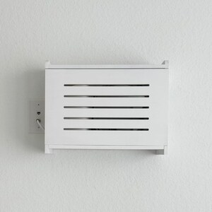 Puede incluir: Un armario blanco rectangular montado en la pared con listones horizontales. El armario est&aacute; montado en una pared blanca, con una toma de corriente el&eacute;ctrica visible a la izquierda. El texto "ZivlynDesigns" est&aacute; en las esquinas superior izquierda e inferior derecha.