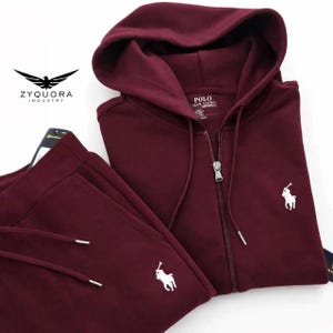 Puede incluir: Un conjunto de chándal burdeos con una chaqueta con capucha y cremallera y pantalones de chándal a juego. La chaqueta y los pantalones tienen cordones blancos y un logotipo blanco de una persona a caballo. La chaqueta tiene el texto "POLO RALPH LAUREN". También es visible la marca "ZYQUORA INDUSTRY".