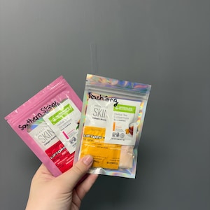 May include: Two packets of Herbalife products are held in a hand. One pink packet is labeled "Southern Skin" and the other is a holographic packet labeled "Finch Ring". Both packets contain "Skin Collagen Beauty" and "Herbal Tea Concentrate".