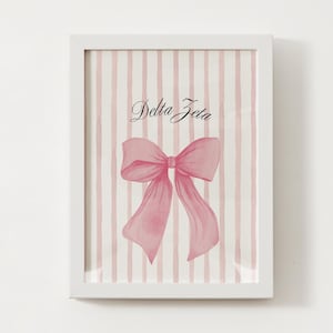 Puede incluir: Impresión enmarcada con un lazo rosa y la inscripción "Delta Zeta". El fondo tiene rayas verticales rosas y blancas. La obra de arte está en un marco blanco.