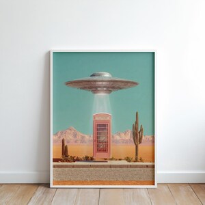 May include: A framed art print featuring a retro-style scene with a pink telephone booth in a desert landscape. A silver UFO hovers above, emitting a bright light. The background includes mountains, cacti, and a teal sky.