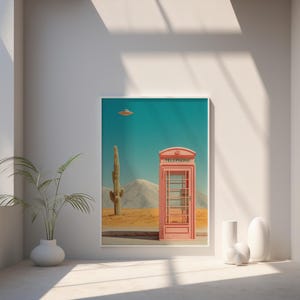 May include: A framed art print featuring a pink telephone booth in a desert landscape with a cactus and a UFO. The word "TELEPHONE" is printed on the top of the booth. The sky is teal.