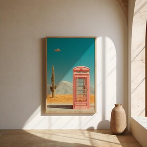 May include: A framed art print featuring a pink telephone booth in a desert landscape under a teal sky. A cactus and a mountain range are visible. The word "TELEPHONE" is printed on the top of the booth. A UFO hovers in the sky.