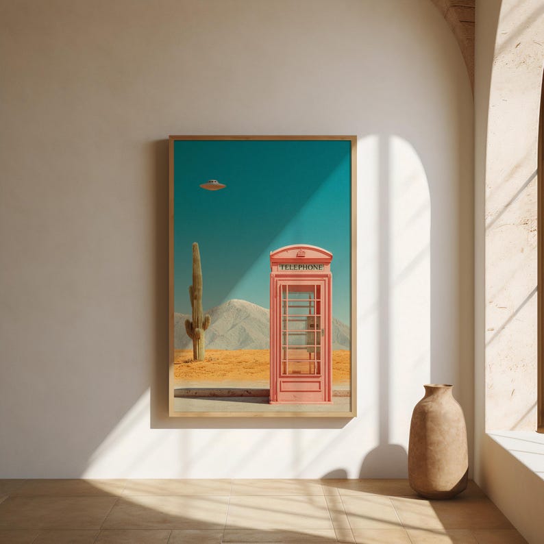 May include: A framed art print featuring a pink telephone booth in a desert landscape under a teal sky. A cactus and a mountain range are visible. The word "TELEPHONE" is printed on the top of the booth. A UFO hovers in the sky.