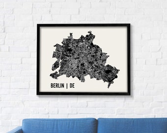 Może przedstawiać: Czarno-biały wydruk mapy Berlina, Niemcy, w czarnej ramie. Mapa przedstawia ulice i zabytki miasta. Tekst "BERLIN | DE" jest wydrukowany pod mapą.
