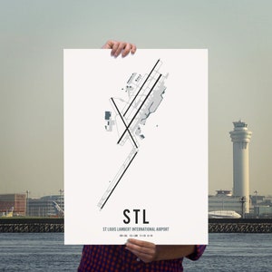 May include: A black and white print of the St. Louis Lambert International Airport (STL) runway layout. The print features the airport code "STL" and the airport name below the runway layout.