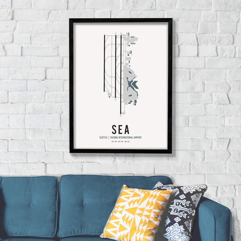 K&ouml;nnte beinhalten: Ein schwarzer gerahmter Druck mit wei&szlig;em Hintergrund und einem grauen und blauen Flughafenlayout. Der Text "SEA" ist in gro&szlig;en, fetten, blauen Buchstaben. Unter dem Flughafenlayout steht der Text "Seattle | Tacoma International Airport".