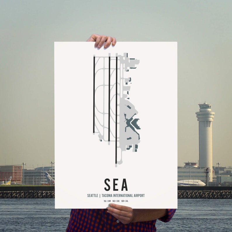 K&ouml;nnte beinhalten: Ein wei&szlig;er Poster mit einer schwarz-grauen Illustration des Flughafens Seattle-Tacoma International Airport (SEA) mit dem Layout der Landebahnen. Der Poster tr&auml;gt den Text "SEA" und "Seattle | Tacoma International Airport" in schwarzer Schrift.