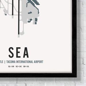 K&ouml;nnte beinhalten: Eine Schwarzwei&szlig;karte eines Flughafens mit dem Text "SEA" und "Seattle | Tacoma International Airport" darunter. Die Karte zeigt die Anordnung des Flughafens mit Start- und Landebahnen sowie Rollwegen. Der Text "16L &bull; 34R 16C &bull; 34C 16R &bull; 34L" befindet sich unter dem Flughafennamen.