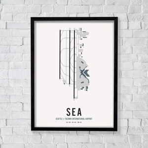 K&ouml;nnte beinhalten: Ein Schwarzwei&szlig;-Druck einer Flughafenkarte mit dem Text "SEA" und "Seattle | Tacoma International Airport" im minimalistischen Stil. Der Flughafencode "SEA" ist in einer gr&ouml;&szlig;eren Schriftgr&ouml;&szlig;e als der Flughafenname.
