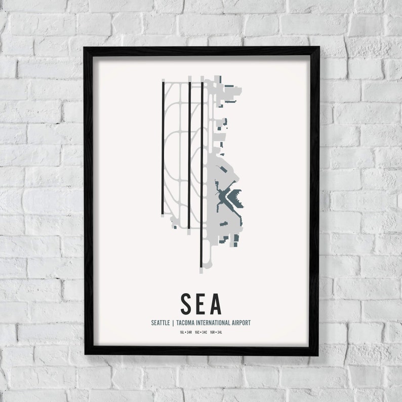 K&ouml;nnte beinhalten: Ein Schwarzwei&szlig;-Druck einer Flughafenkarte mit dem Text "SEA" und "Seattle | Tacoma International Airport" im minimalistischen Stil. Der Flughafencode "SEA" ist in einer gr&ouml;&szlig;eren Schriftgr&ouml;&szlig;e als der Flughafenname.