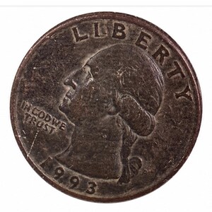 May include: A dark, weathered United States quarter coin featuring the profile of George Washington facing left. The text LIBERTY is arched across the top, IN GOD WE TRUST is on the left, and the year 1993 is printed at the bottom of the coin.