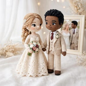Op de afbeelding: Gehaakte bruidspoppen van een bruid en bruidegom. De bruid draagt een crèmekleurige jurk en houdt een boeket vast. De bruidegom draagt een beige pak met een rode stropdas. Een ingelijste foto van een stel staat op de achtergrond.