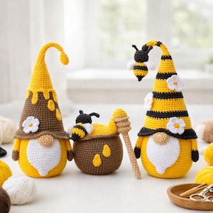 May include: A collection of crocheted bee-themed ornaments. The gnomes feature yellow and brown hats, white beards, and small white flowers. A brown honey pot with yellow details and a wooden dipper is also present. A small crocheted bee hovers above one gnome.