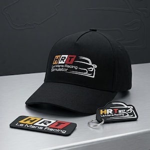 Può includere: Un cappellino da baseball nero con un logo ricamato che riporta il testo HRT Le Mans Racing Simulator e il contorno bianco di un'auto. Accanto si trovano una toppa rettangolare nera e un portachiavi nero, entrambi con il logo HRT Le Mans Racing.