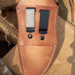 May include: A white ceramic mug with a black handle and the text "But First, Coffee" in a bold, black font. The mug is set against a blurred background, suggesting a cozy setting.