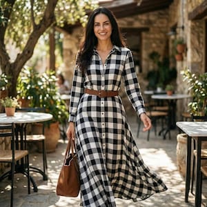 May include: A long-sleeved black and white checkered dress with a brown belt and a brown tote bag. The dress has a button-down front and a flowing skirt. The woman is smiling and walking outside.