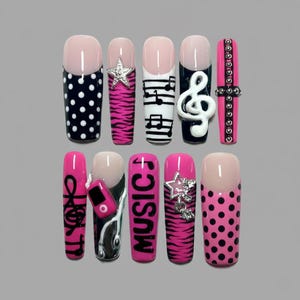 May include: A set of ten long, artificial nails with various designs. The nails feature black and white polka dots, pink zebra stripes, musical notes, a treble clef, and the word "MUSIC". Some nails have silver star and stud embellishments.