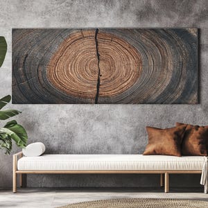 May include: A rectangular wooden wall art piece featuring a cross-section of a tree trunk. The artwork displays concentric rings in shades of brown and gray, with a prominent vertical crack. The piece is mounted on a gray wall.