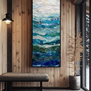 May include: A framed abstract art piece depicting a layered ocean scene. The artwork features shades of blue, teal, and green, with white accents, creating a textured, wave-like effect. The piece is displayed in a rustic interior setting with wood paneling.