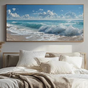 Puede incluir: Impresión en lienzo enmarcada que representa una escena costera. La obra de arte muestra un mar turquesa con olas espumosas rompiendo en una playa de arena bajo un cielo azul con nubes blancas. El marco es de color marrón claro.