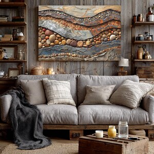 May include: A living room scene featuring a gray sofa with several pillows and a dark gray throw blanket. A large abstract artwork with layered textures and earth-tone colors hangs above the sofa. A wooden crate serves as a coffee table, and a jute rug covers the floor.