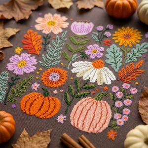 May include: A cross-stitch embroidery on dark brown fabric featuring a seasonal arrangement of orange and peach pumpkins, various autumn leaves in shades of orange and green, and a collection of flowers in pink, white, and yellow hues.