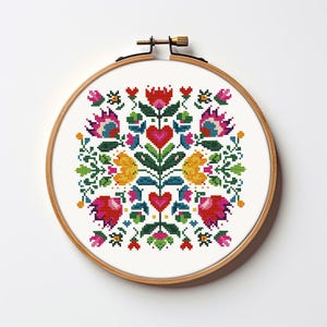 May include: A colorful cross-stitch design featuring a floral pattern with red hearts, yellow and pink flowers, and green leaves. The embroidery is set in a round wooden hoop, perfect for wall decor or a handmade gift.