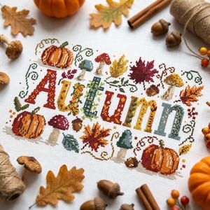 K&ouml;nnte beinhalten: Ein Kreuzstich-Stickbild auf wei&szlig;em Stoff mit dem Wort Autumn in gro&szlig;en, bunten Buchstaben, umgeben von gestickten K&uuml;rbissen, Pilzen, Eicheln und verschiedenen Herbstbl&auml;ttern, akzentuiert durch echte K&uuml;rbisse und herbstliches Laub.